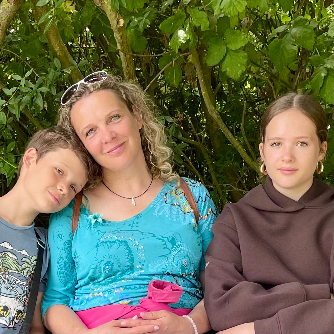 Familie mit Mutter, Sohn und Tochter, sitzen nebeneinander, Sohn legt den Kopf auf die Schulter der Mutter