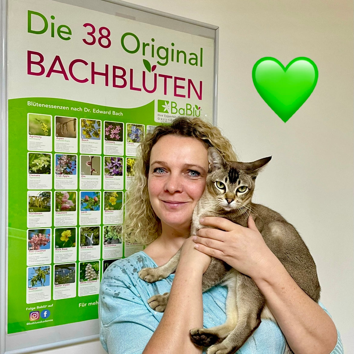 Portrait von einer Frau, die eine braune Katze am Arm hält, im Hintergrund ein Poster mit Bachblüten